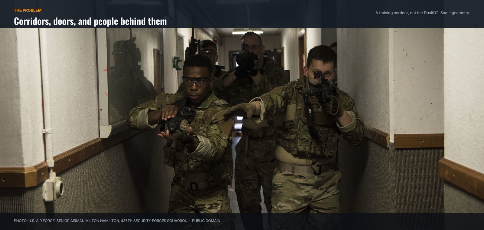 A team of airmen with carbines advancing down a narrow hotel style corridor during close quarters battle training