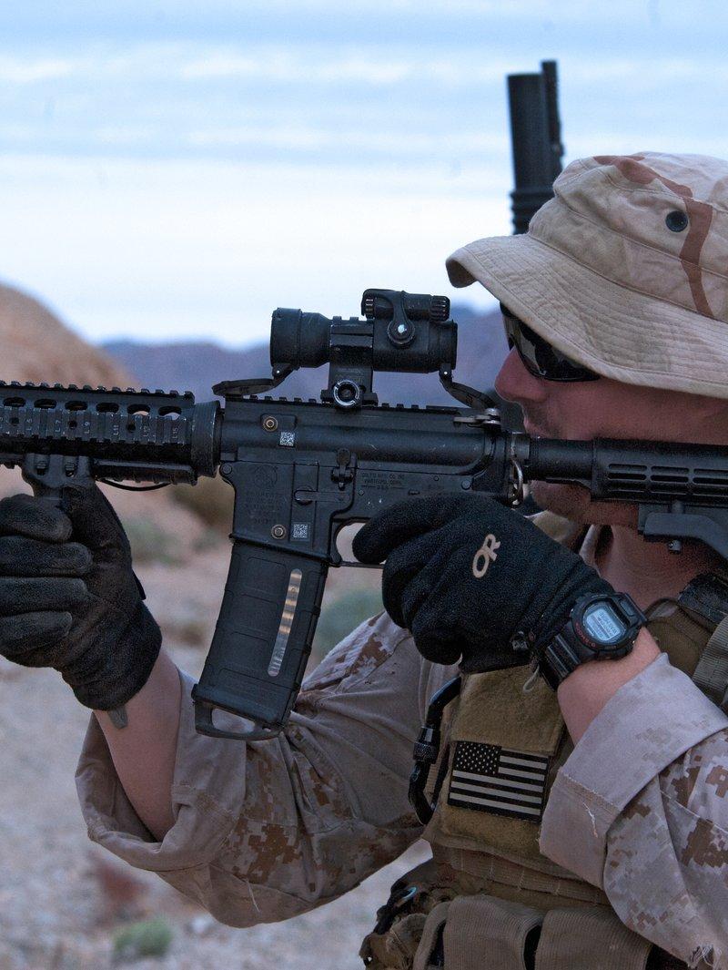 Navy SEAL in desert camouflage aiming a short CQBR carbine with a quad rail, fixed front sight, vertical foregrip and red dot sight
