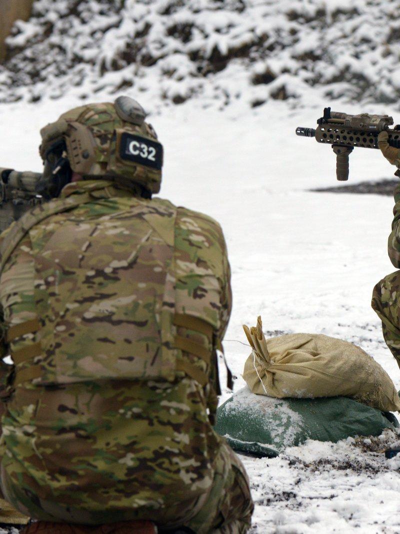 Two 10th Special Forces Group soldiers kneel on a snowy range aiming M4A1 carbines with long tan quad rails, a front sight post rising through the rail on the right