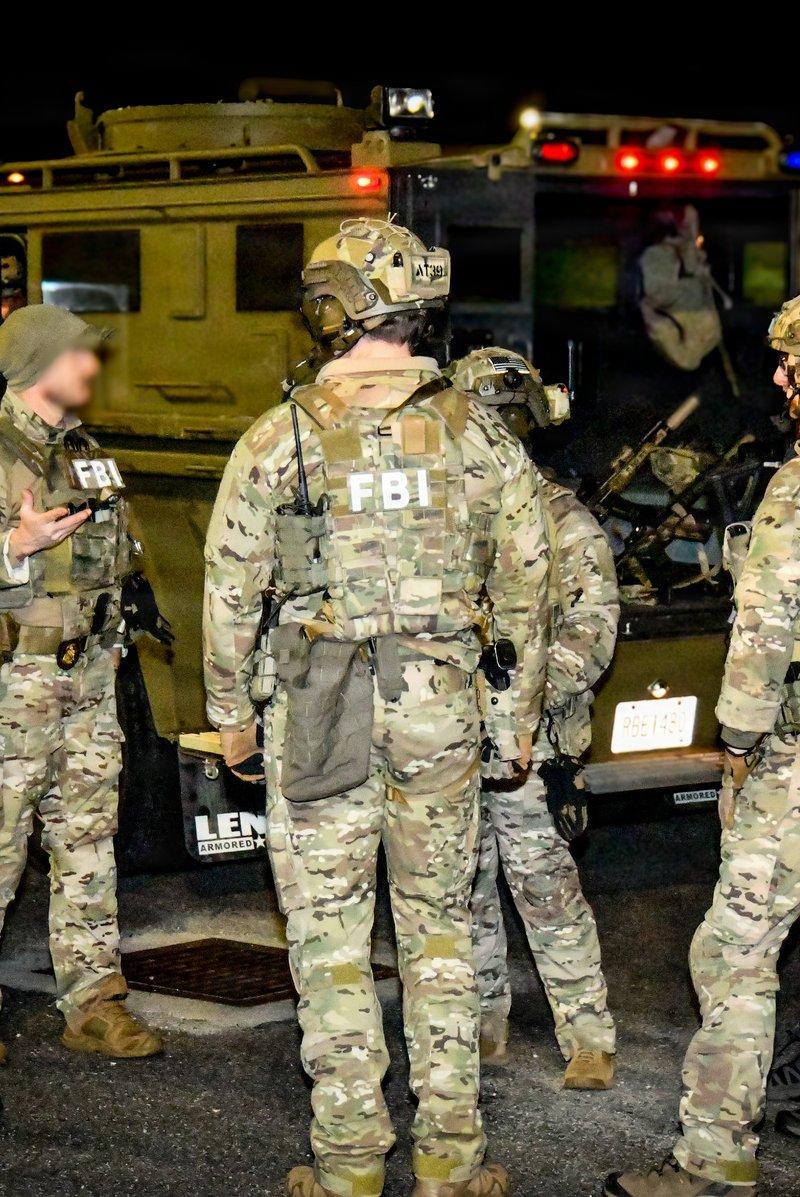 FBI Atlanta agents in Multicam and FBI marked plate carriers stand at night beside a Lenco armored truck, with a suppressed carbine visible inside the open vehicle