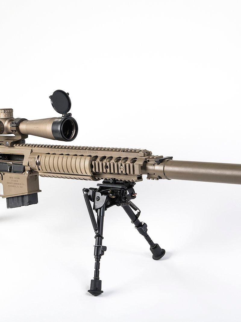 Un rifle de francotirador M110 del Ejército color tan sobre fondo blanco con una mira en montura de una pieza, un guardamanos con rieles, un supresor largo y un bípode plegable