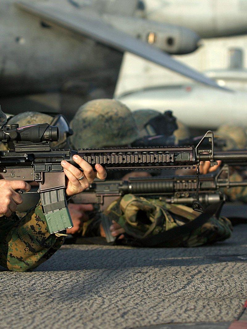 A prone Marine on a ship's deck aims an M16A4 with an ACOG