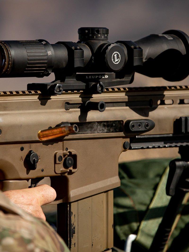 Close view of a Green Beret aiming a flat dark earth Mk17 with a Leupold scope in a one piece mount and a bipod, a spent case flying from the ejection port