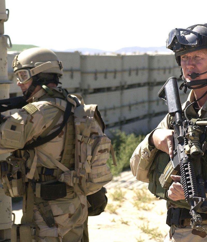 Two Navy SEALs in desert camouflage cover a mock embassy compound with short barreled carbines fitted with Knight's Armament quad rails