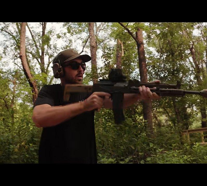 Shooter firing the PSA Sabre 5.56 AK with a suppressor mounted, outdoor range
